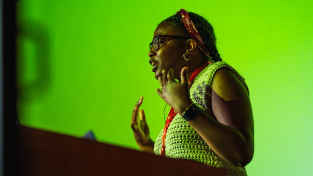 Lola Odelola presenting at a conference event, appearing to speak passionately an emoting with her hands